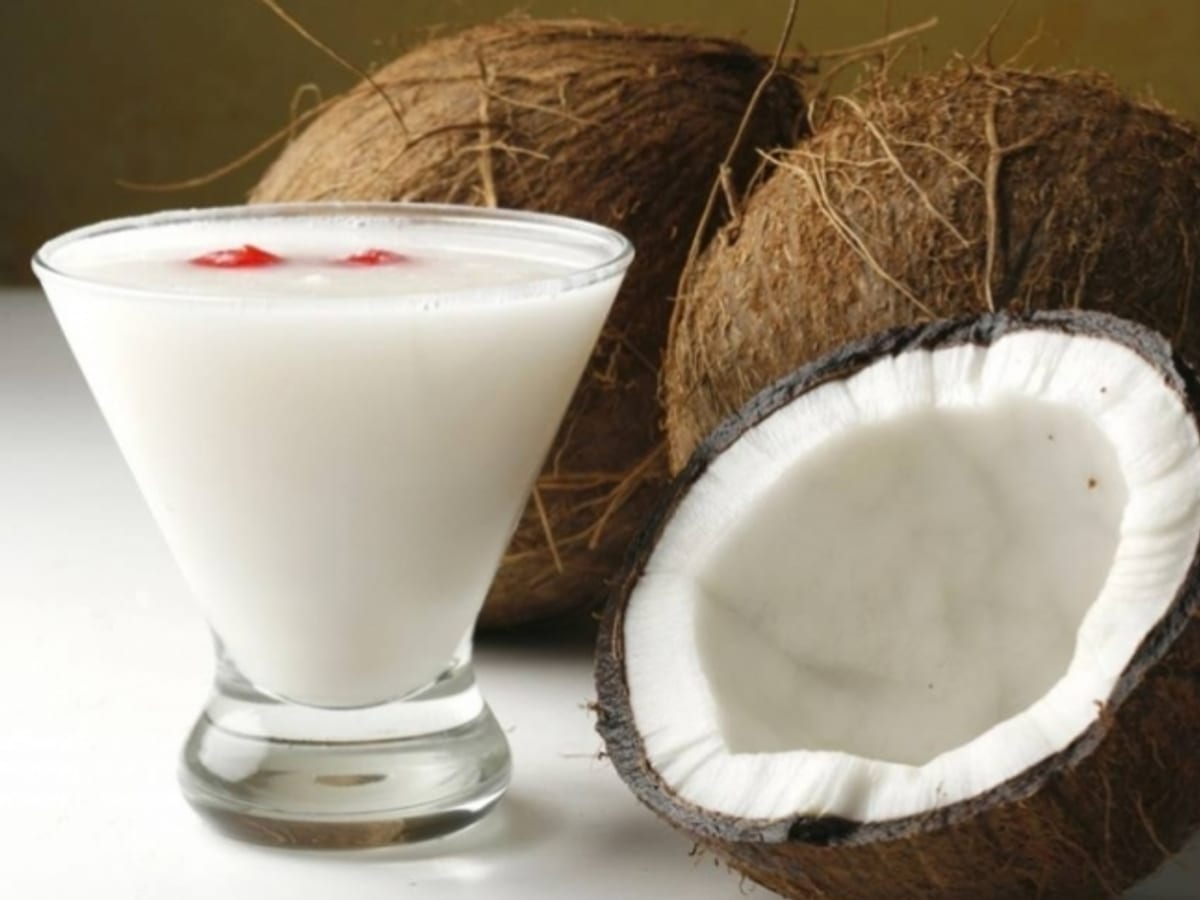 Vaso de cocada cremosa junto a un coco entero y otro partido a la mitad