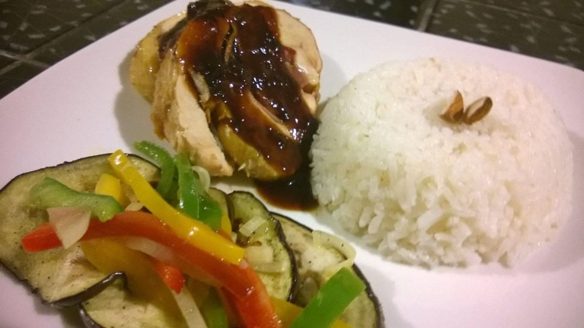 Ballotine de pollo en rodajas bañado en salsa oscura, servido con arroz blanco y berenjenas asadas