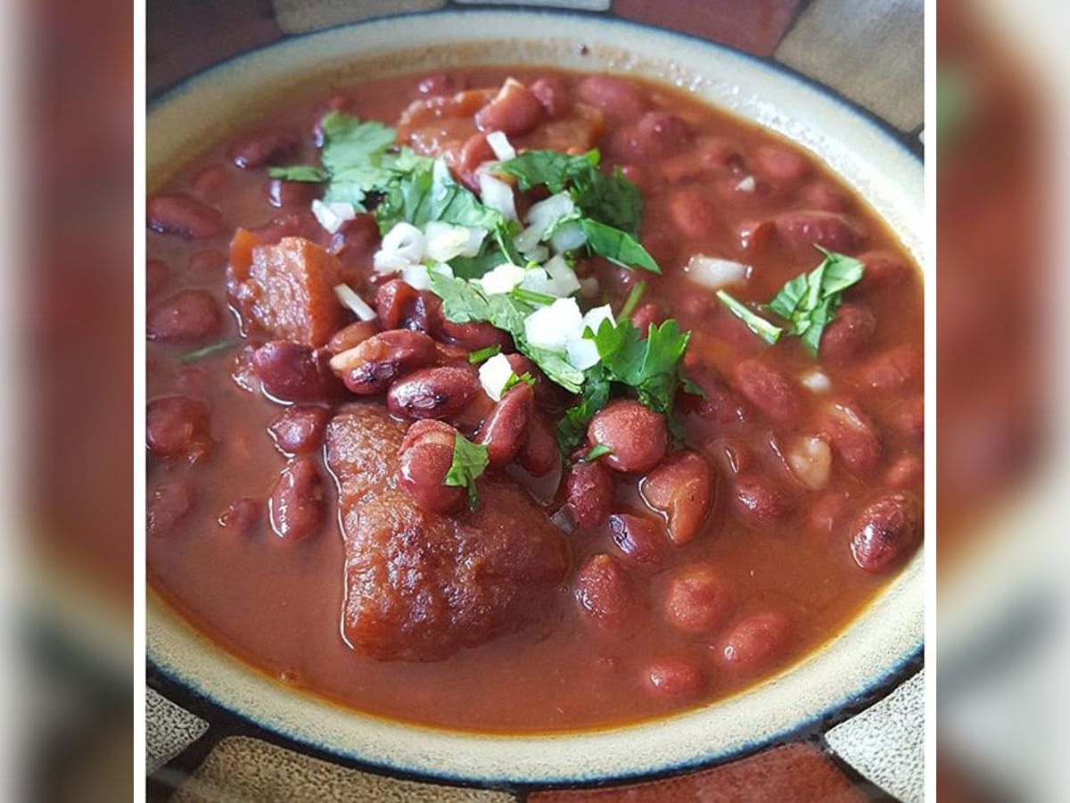 Frijoles con chicharrón servidos en un plato hondo, con cilantro y cebolla picados