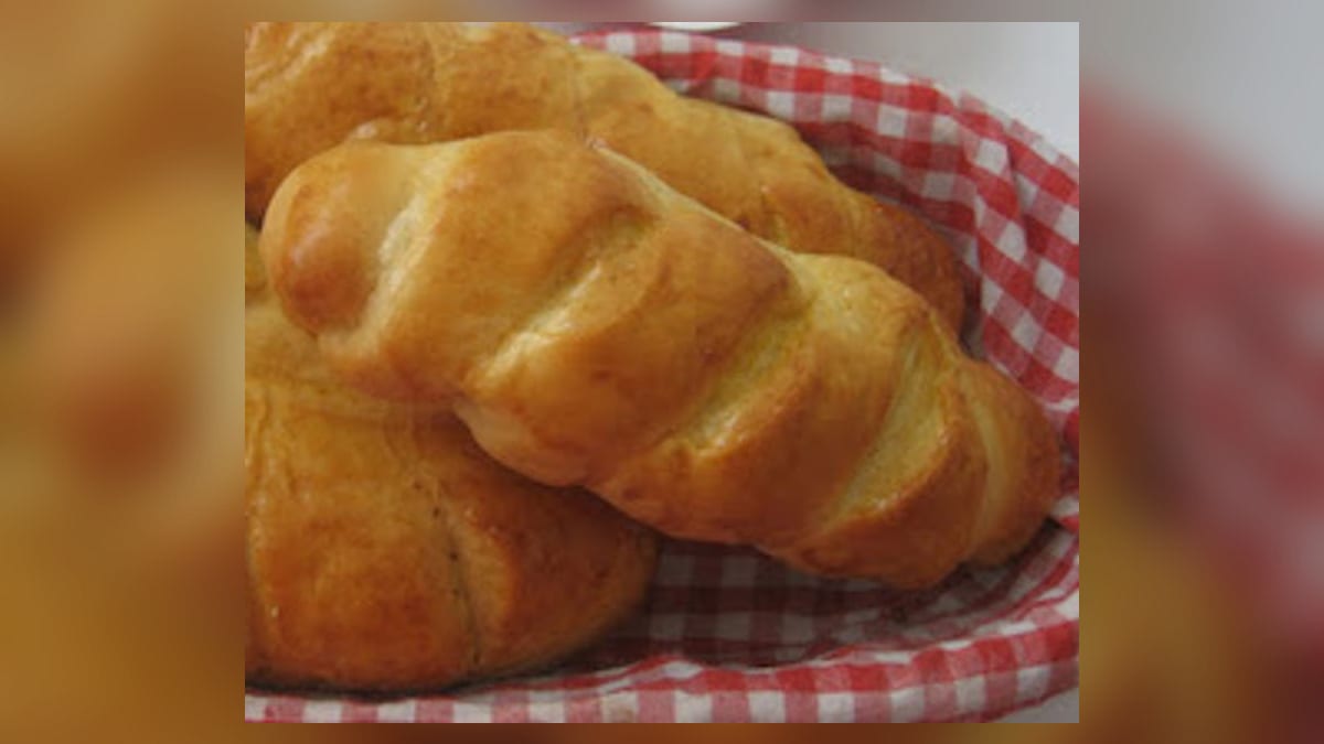 Panes de queso trenzados y dorados, servidos en una cesta forrada con tela a cuadros