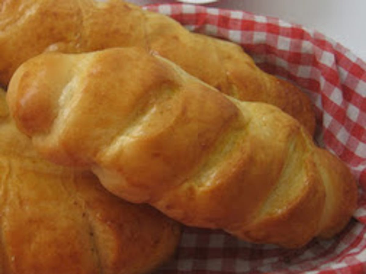 Panes de queso trenzados y dorados, servidos en una cesta forrada con tela a cuadros