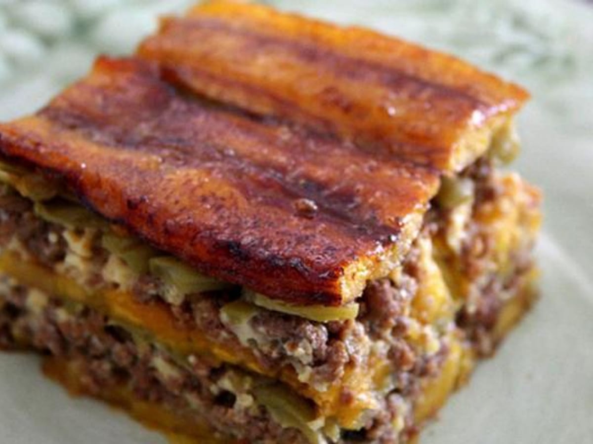 Porción de pasticho de plátano maduro con capas de carne molida, queso y jamón, gratinado al horno